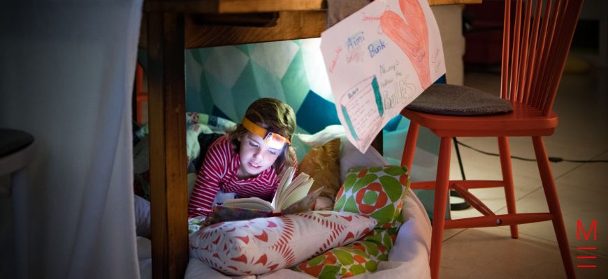 A young girl reading in her pillow fort