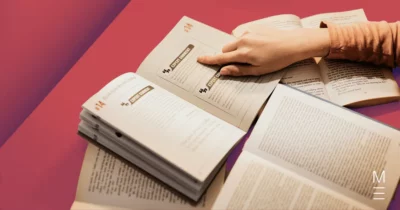 Hand pointing to text in an open book, surrounded by study materials