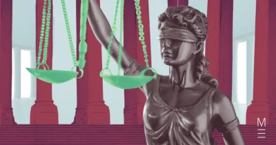 Lady Justice statue holding green scales against a background of red pillars