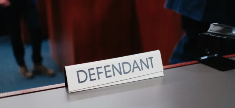 a desk nameplate that reads "Defendant" in a courtroom, representing a legal proceeding