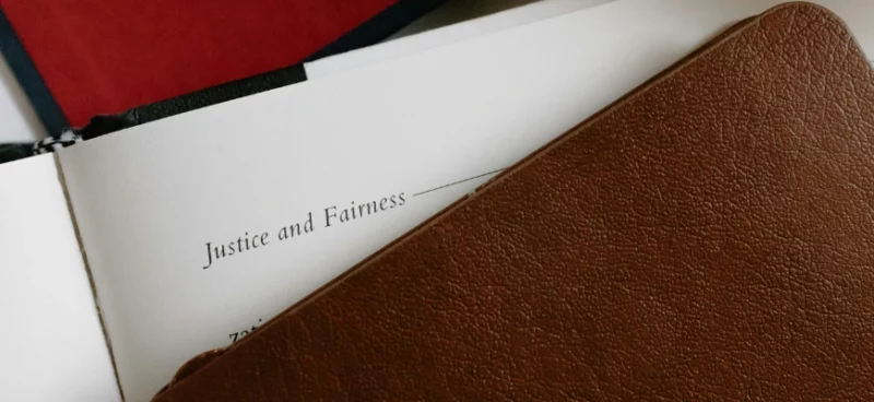 A leather notebook partially covering a page with the words "Justice and Fairness"