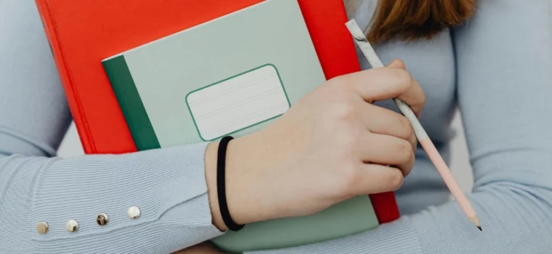 Student holding notebooks and a pencil, ready for study.