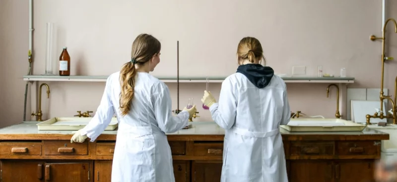 Two students in lab coats working in a chemistry laboratory
