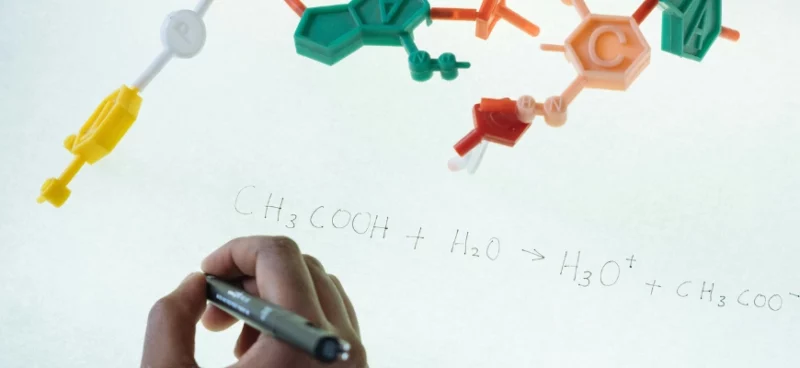 Student writing a chemical equation with molecular model pieces