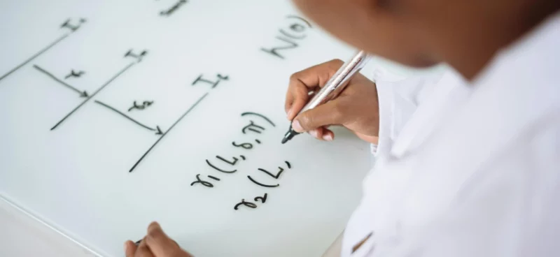 Student writing physics equations on a whiteboard