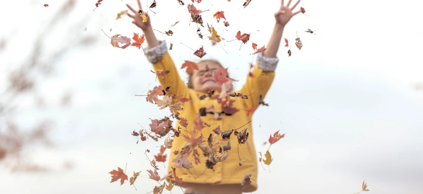 child throwing brown leaves into the air