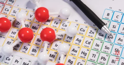 A molecular model with red and white atoms placed over a periodic table