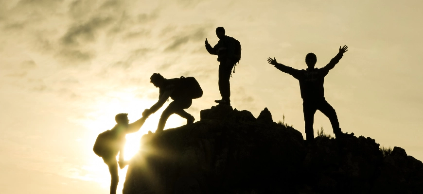 matrix education group of people silhouetted against a sunset, helping each other climb a hill