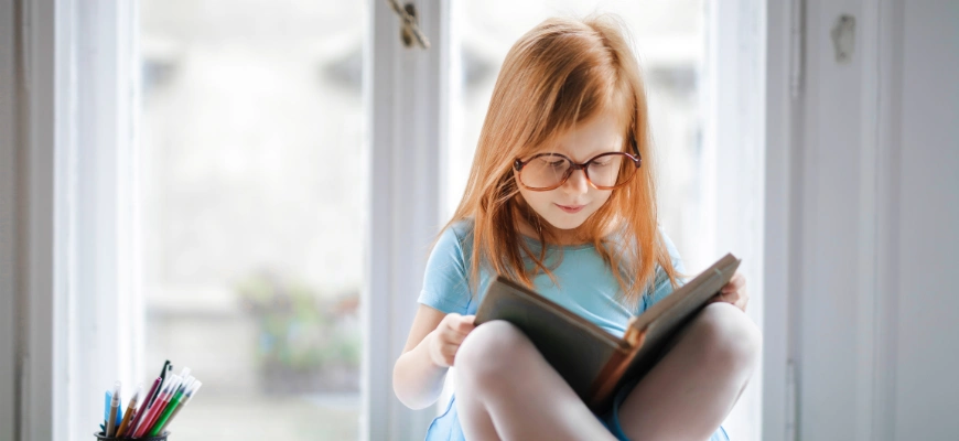 matrix education A young girl with red hair reading a book by a window.