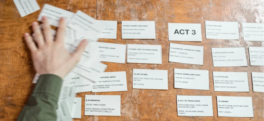 A person arranging story planning cards on a wooden table.