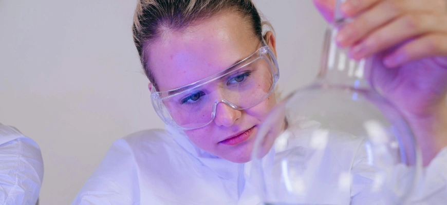 A student in safety goggles carefully examining a laboratory flask.