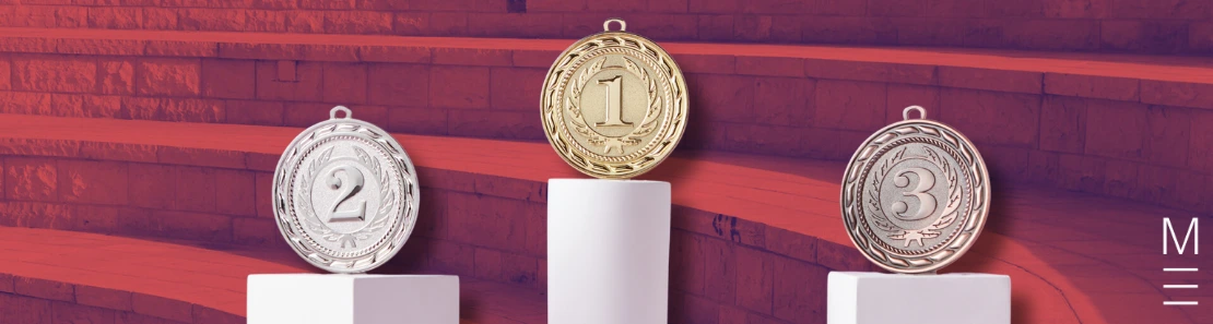 A podium with gold, silver, and bronze medals on white pedestals against a background featuring stadium steps