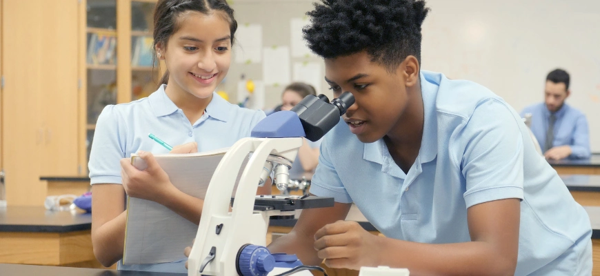 matrix education boy looking through a microscope in a school lab, a girl next to him writes notes