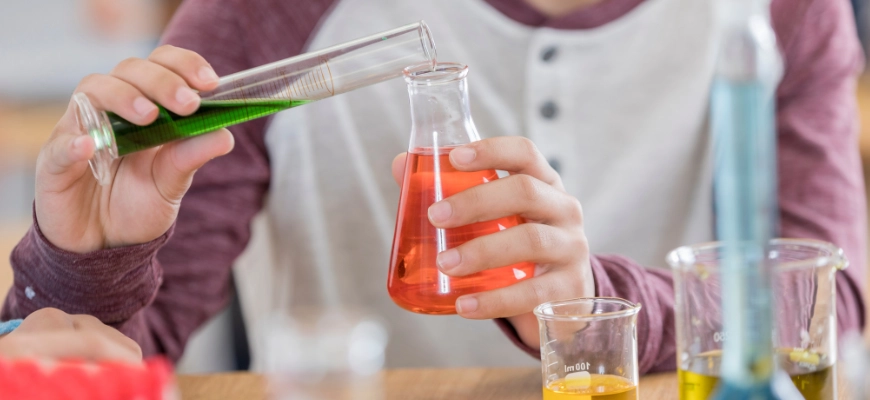 matrix education A student pouring green liquid into a flask containing red liquid in a chemistry lab, symbolising redox reaction practice.