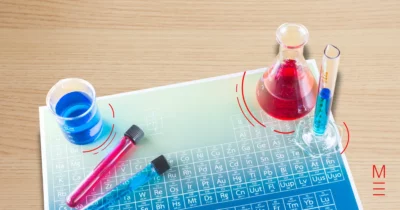 Periodic table under colourful beakers containing red and blue liquids
