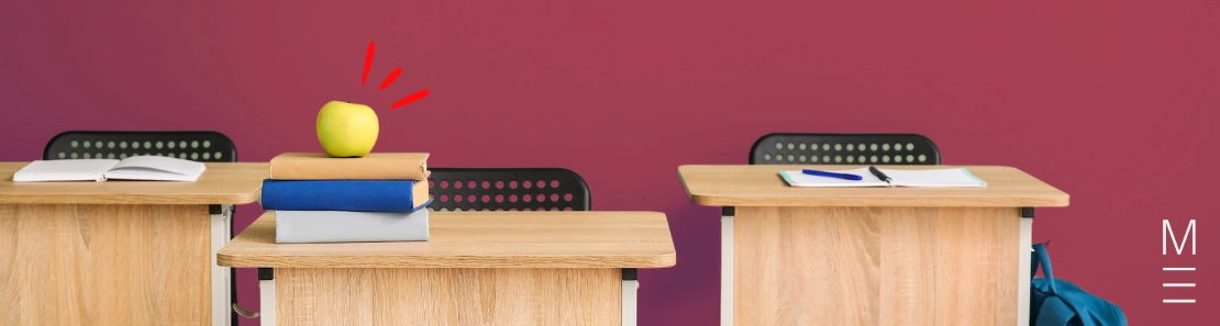 Wooden school desks with books, an apple, and stationery placed on top