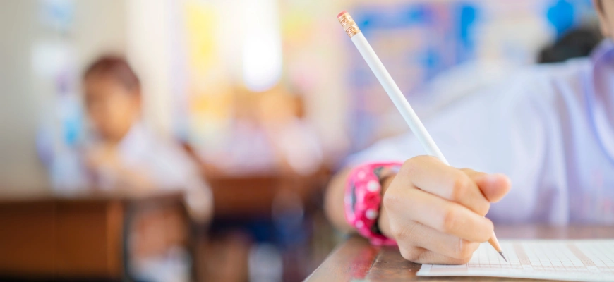 Close-up of a student's hand holding a pencil while writing on a test paper symbolising private school scholarship exams