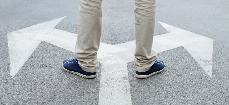 Person standing at a fork in the road with large white arrows pointing in different directions