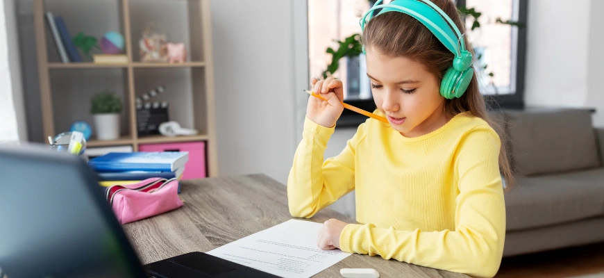 Girl in headphones studying with a worksheet and laptop.